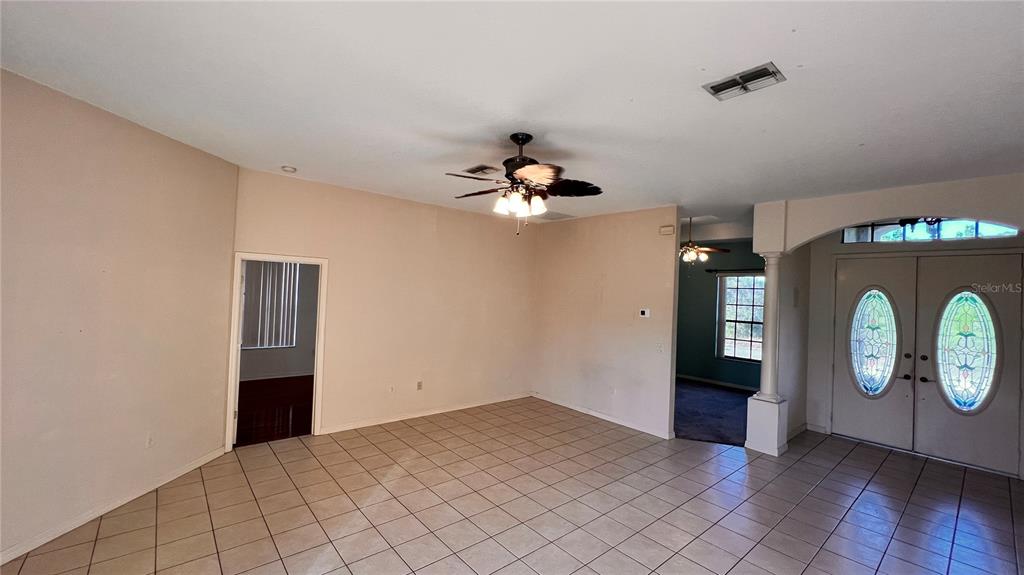 A living room with beige walls, tile flooring, a ceiling fan, and double front doors — 9140 LAMBORN STREET, SPRING HILL, FL