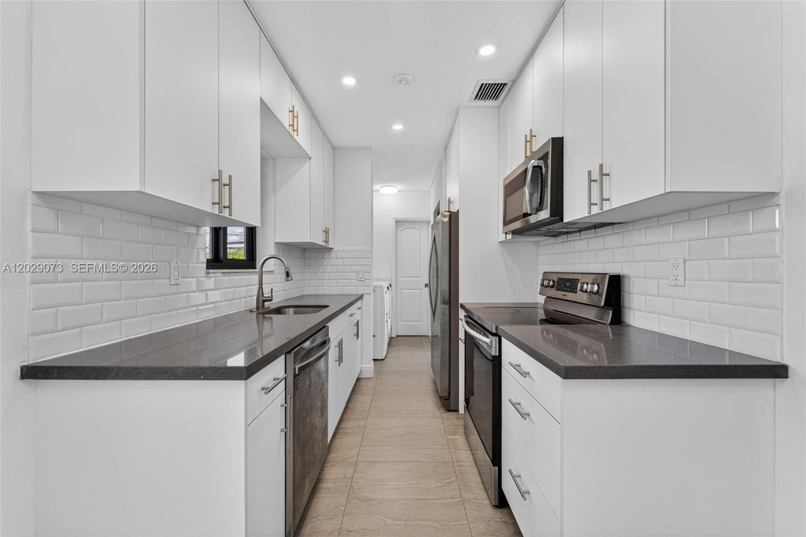 A galley kitchen features white cabinets, dark gray countertops, and white subway tile backsplashes — 680 W 50th Pl, Hialeah FL 33012, HIALEAH, FL