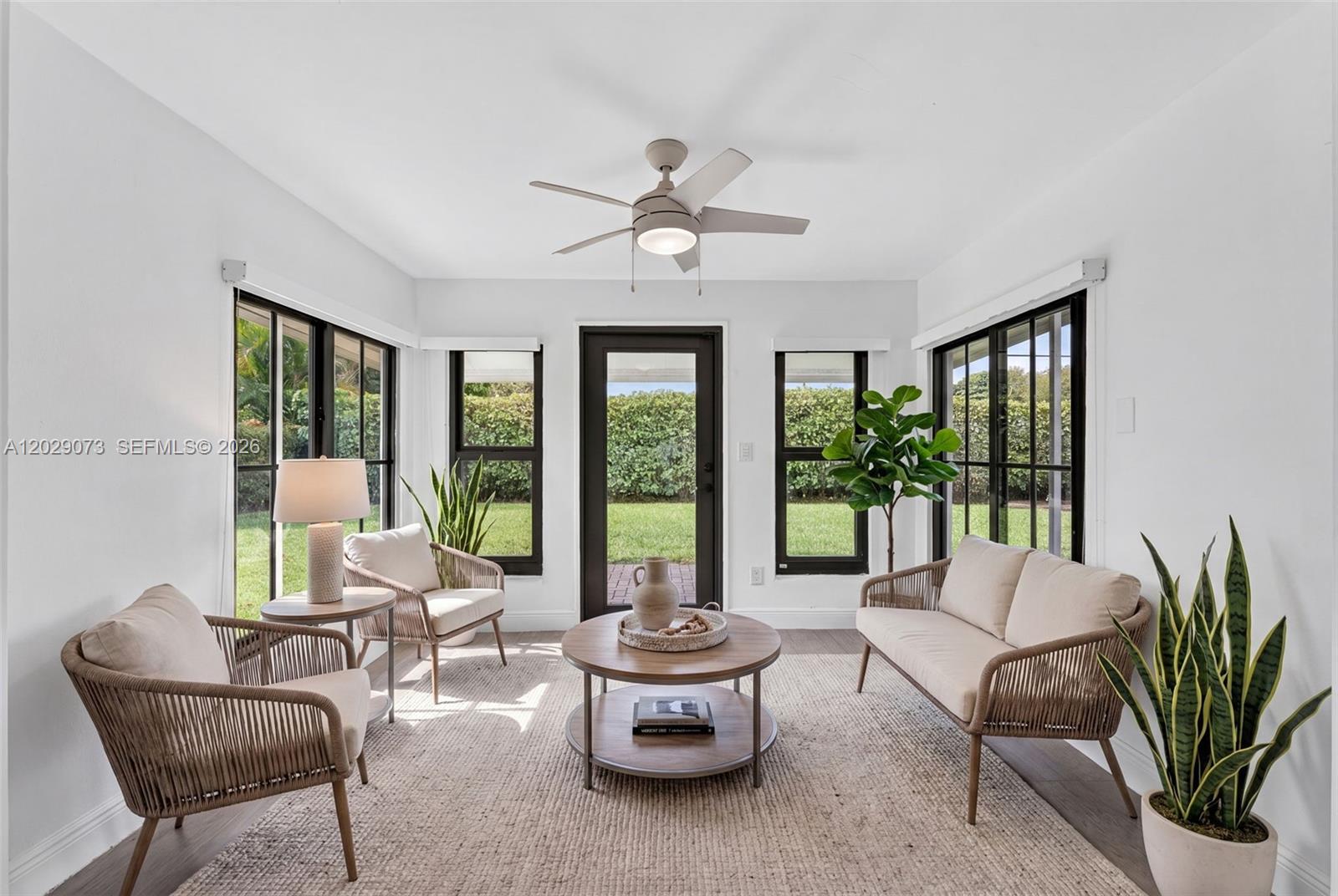 A sunroom features wicker furniture, a round coffee table, and large windows overlooking a lawn — 680 W 50th Pl, Hialeah FL 33012, HIALEAH, FL