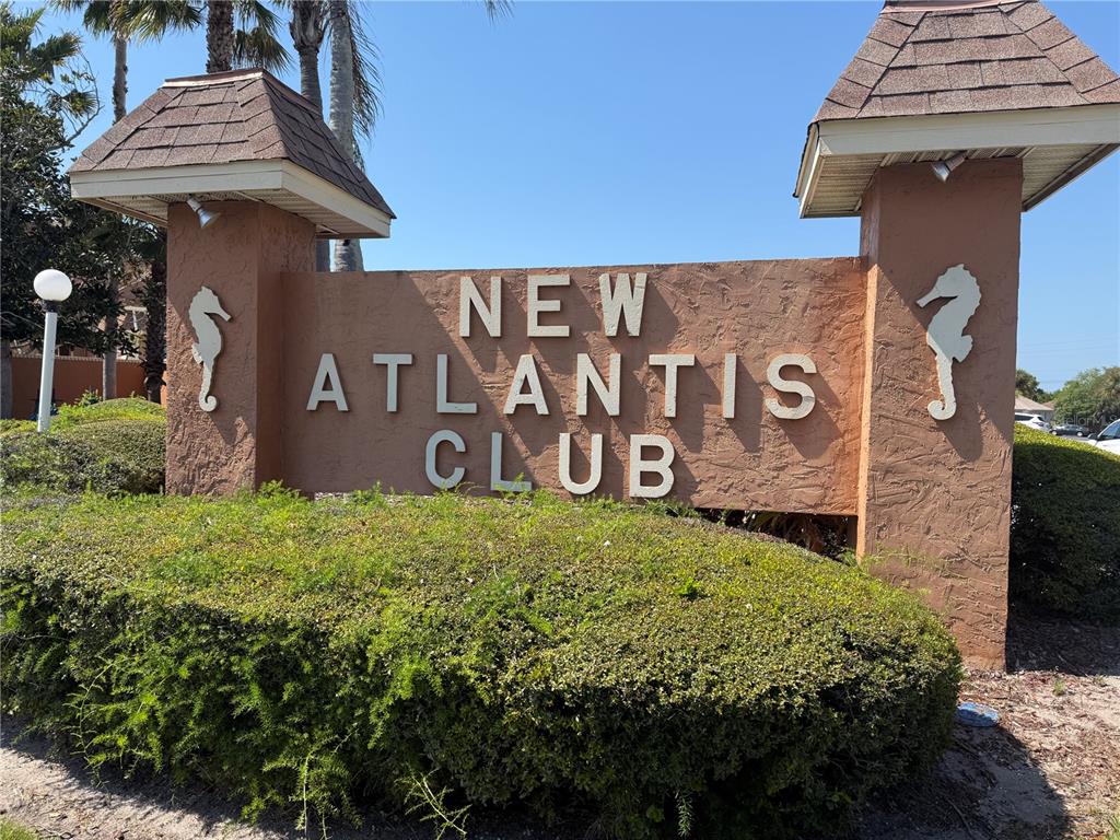 A tan stucco sign for the New Atlantis Club stands behind a manicured green hedge — 12760 INDIAN ROCKS ROAD UNIT 1024, LARGO, FL