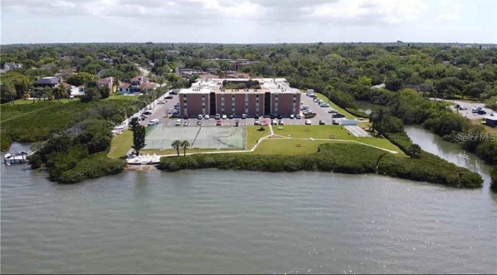 An aerial view shows a multi-story apartment building surrounded by water, trees, and a tennis court — 12760 INDIAN ROCKS ROAD UNIT 1024, LARGO, FL