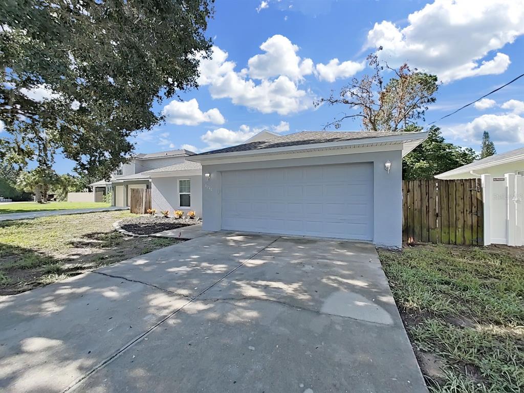 A light gray house features a two-car garage and a concrete driveway under a blue sky — 6240 ARTHUR AVENUE, NEW PORT RICHEY, FL