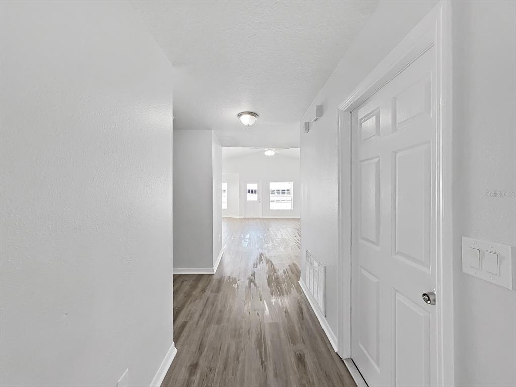 A hallway with light gray walls and wood-look flooring leads toward an open living area — 6240 ARTHUR AVENUE, NEW PORT RICHEY, FL