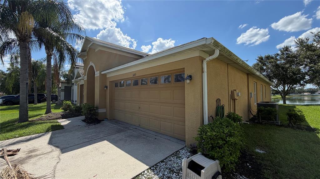 A tan stucco house with a two-car garage and a view of a nearby pond — 31205 BRIDGEGATE DRIVE, WESLEY CHAPEL, FL