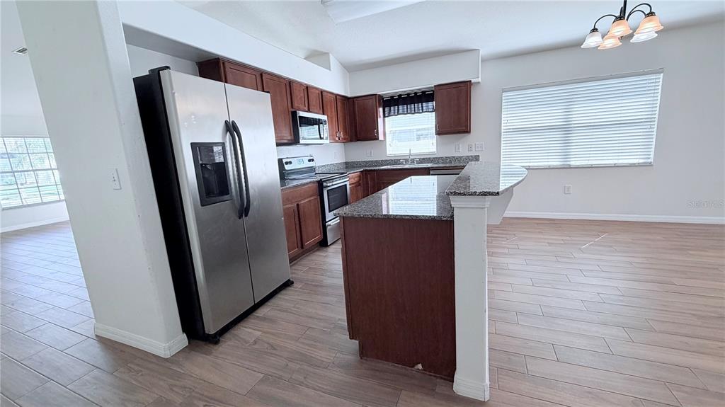 A kitchen features dark wood cabinets, granite countertops, stainless steel appliances, and wood-look tile flooring — 31205 BRIDGEGATE DRIVE, WESLEY CHAPEL, FL