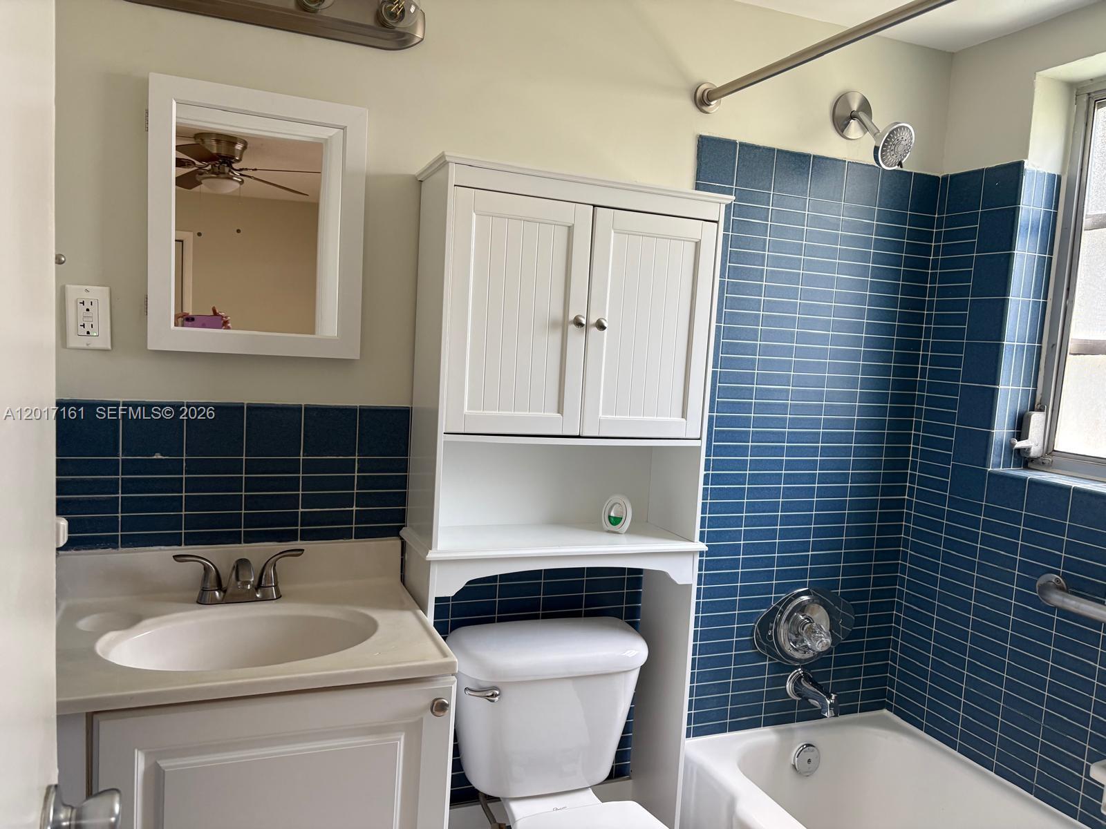 A bathroom features a white vanity, a toilet with an over-the-toilet cabinet, and blue-tiled walls — 3212 NE 7th Pl # 10, Pompano Beach FL 33062, POMPANO BEACH, FL