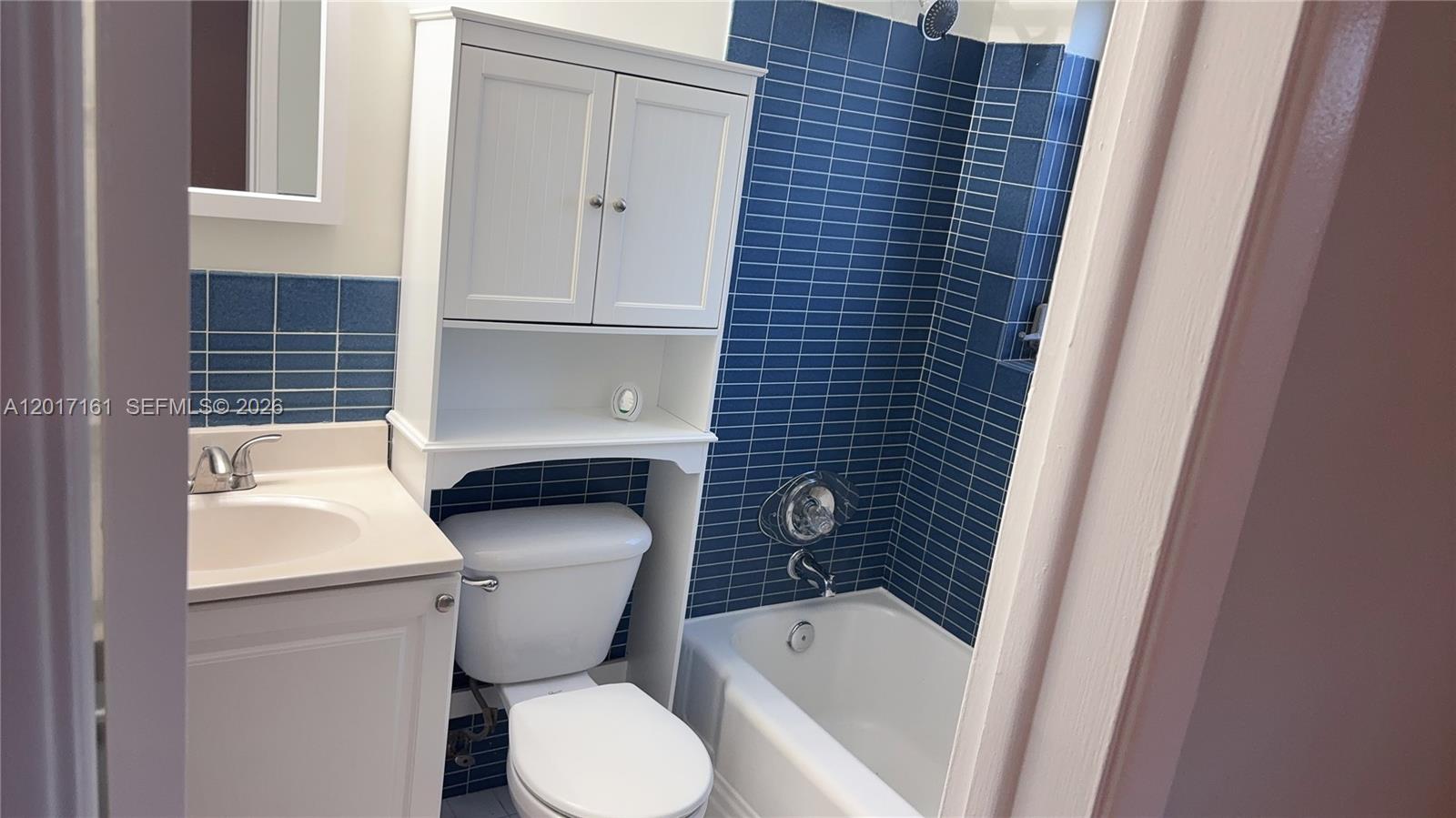 A bathroom features a white vanity, a toilet with an over-the-toilet cabinet, and blue tiles — 3212 NE 7th Pl # 10, Pompano Beach FL 33062, POMPANO BEACH, FL