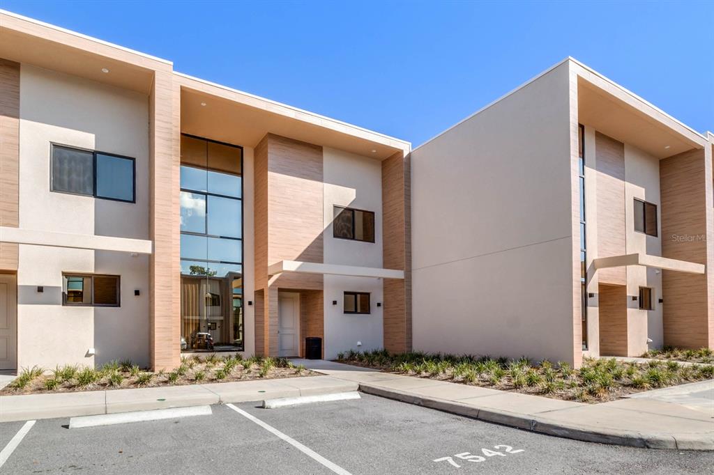 A modern two-story townhouse exterior with beige stucco, wood-look accents, and large glass windows — 7540 BROOKLYN DRIVE, KISSIMMEE, FL