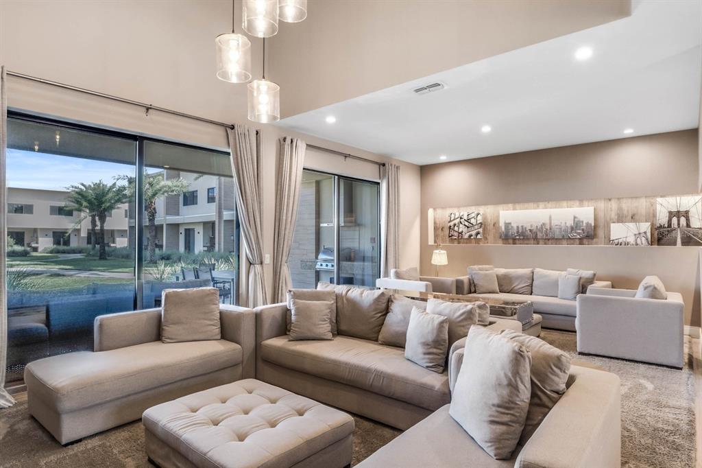A spacious living room features neutral sectional sofas, a tufted ottoman, and large sliding glass doors — 7540 BROOKLYN DRIVE, KISSIMMEE, FL