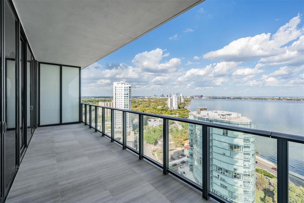 A modern high-rise balcony features gray tile flooring and a glass railing overlooking a city — 3015 S YSABELLA AVENUE UNIT 2003, TAMPA, FL