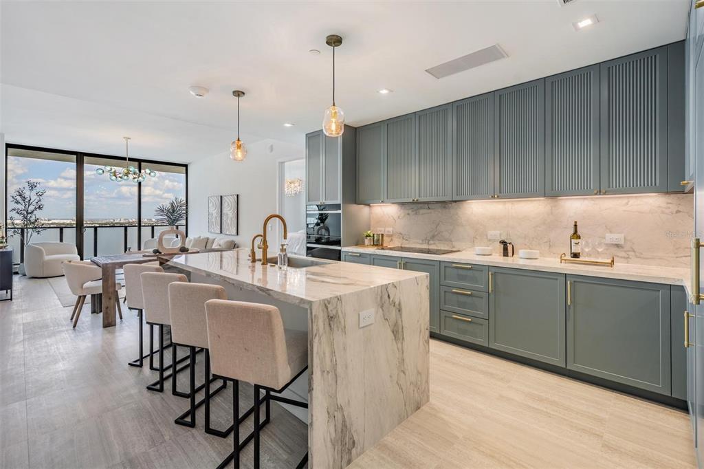 A modern kitchen features a marble waterfall island, sage green cabinetry, and floor-to-ceiling windows — 3015 S YSABELLA AVENUE UNIT 2003, TAMPA, FL