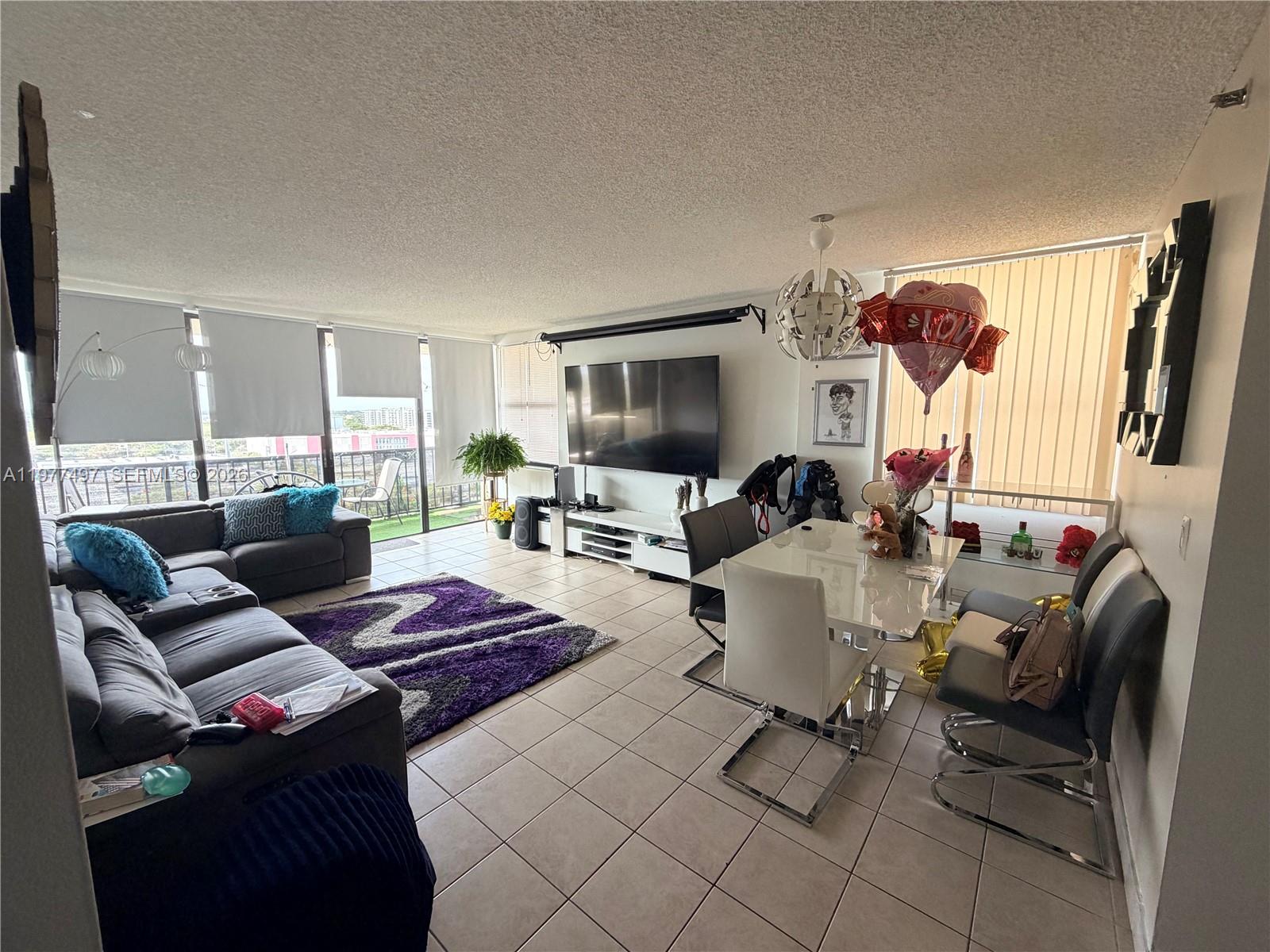 A living and dining area features tile floors, a large sectional sofa, and floor-to-ceiling windows — 1470 NE 123rd St # A1116, North Miami FL 33161, NORTH MIAMI, FL