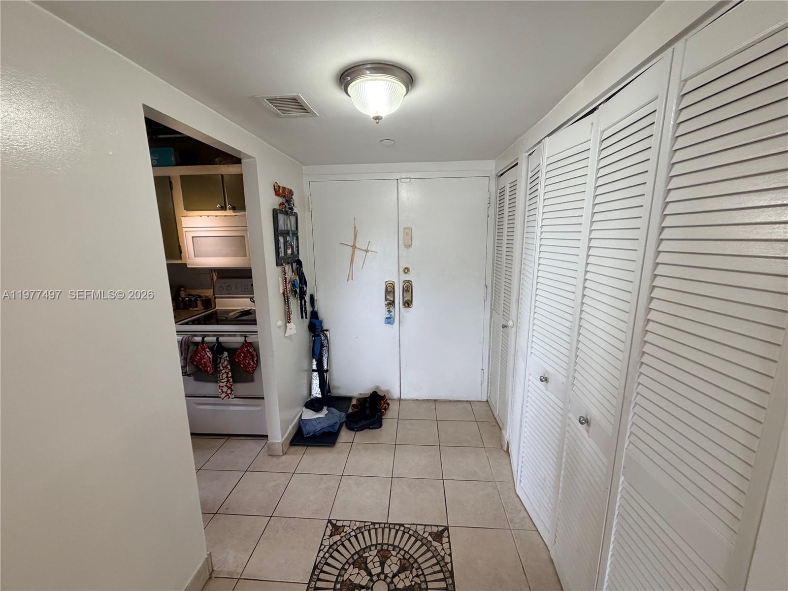An entryway features tiled floors, white louvered closet doors, and a view into a kitchen — 1470 NE 123rd St # A1116, North Miami FL 33161, NORTH MIAMI, FL