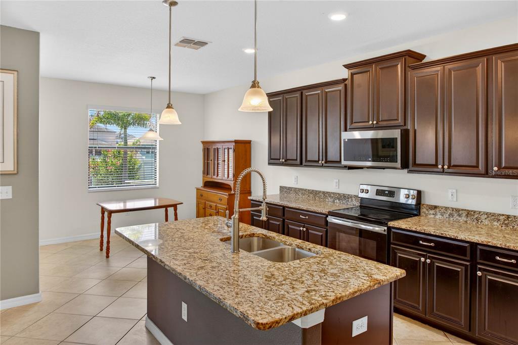 A kitchen featuring dark wood cabinets, granite countertops, a center island, and a dining area — 13415 WHITE SAPPHIRE ROAD, RIVERVIEW, FL