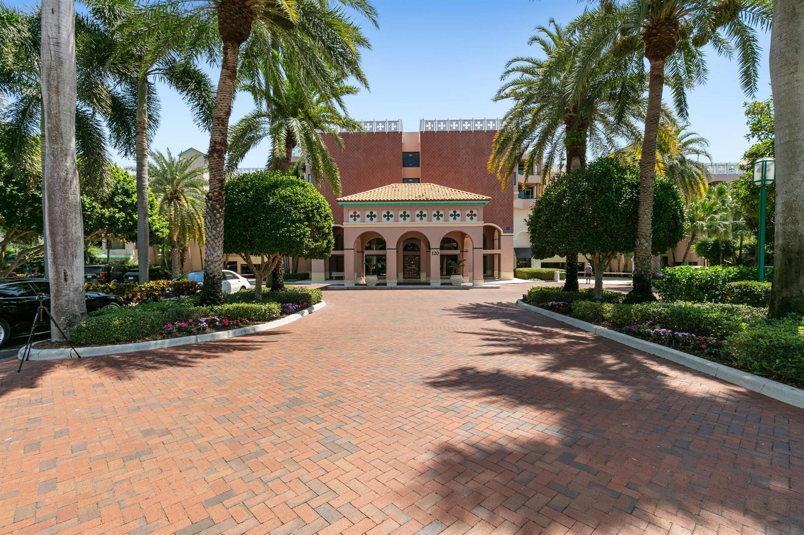 A brick driveway leads to the arched entrance of a multi-story building with palm trees — 120 SE 5th Avenue Apt 128, Boca Raton FL 33432, BOCA RATON, FL
