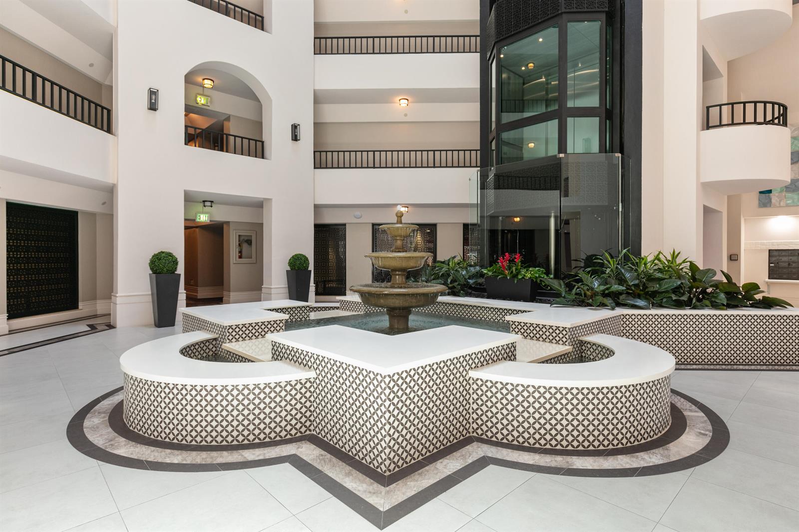 A multi-story atrium features a central tiered fountain surrounded by patterned tile seating — 120 SE 5th Avenue Apt 128, Boca Raton FL 33432, BOCA RATON, FL