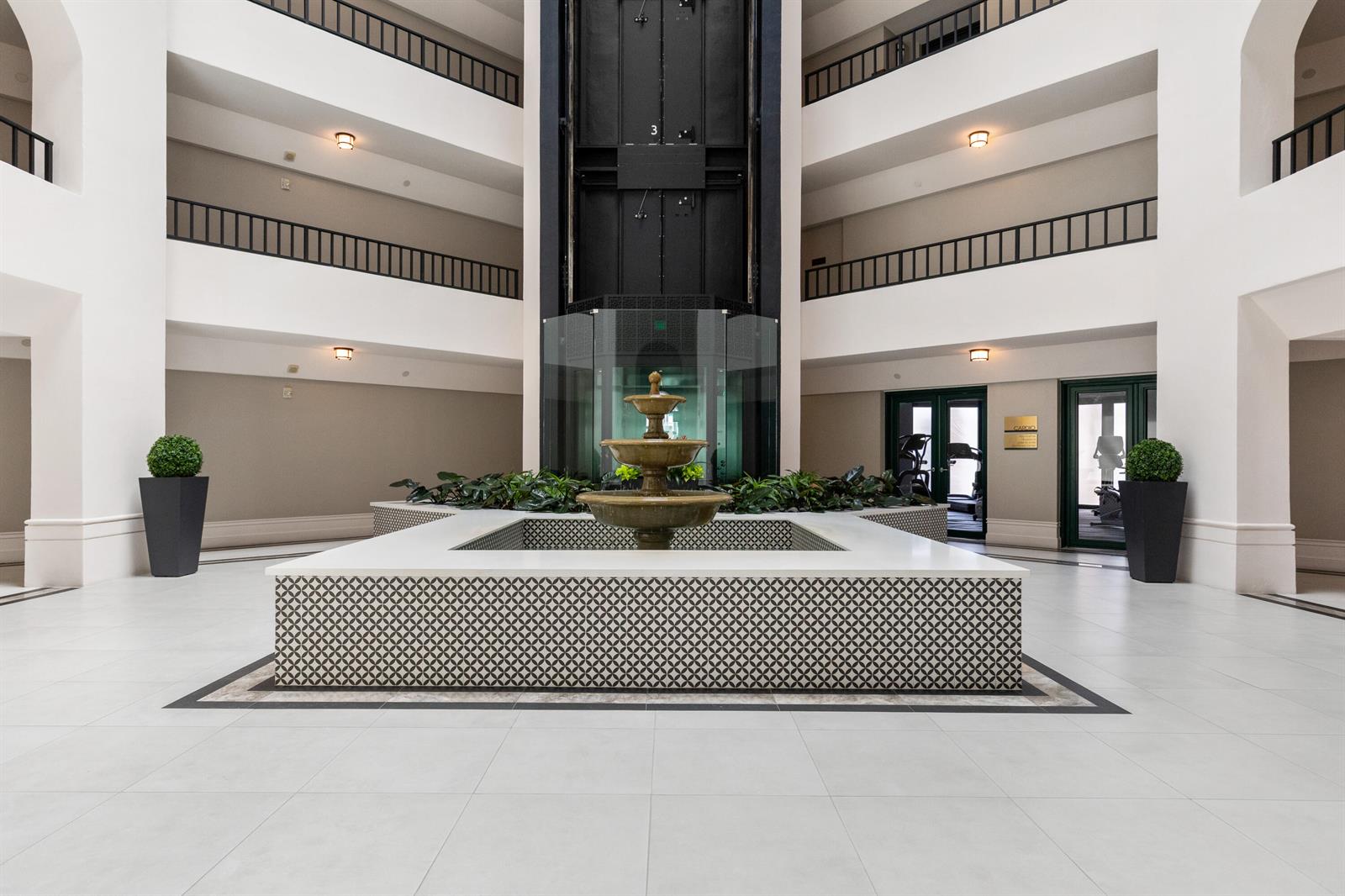 A multi-story atrium features a central tiered fountain, tiled planters, and a glass elevator — 120 SE 5th Avenue Apt 128, Boca Raton FL 33432, BOCA RATON, FL