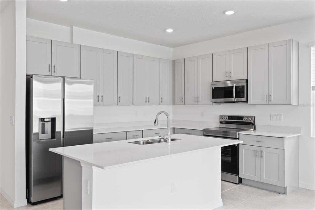 A modern kitchen features light gray cabinets, stainless steel appliances, and a white quartz island — 491 SILVER PALM DRIVE, HAINES CITY, FL