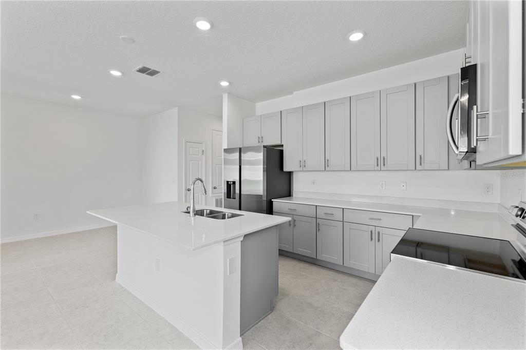 A modern kitchen features gray cabinets, white countertops, a central island, and stainless steel appliances — 491 SILVER PALM DRIVE, HAINES CITY, FL