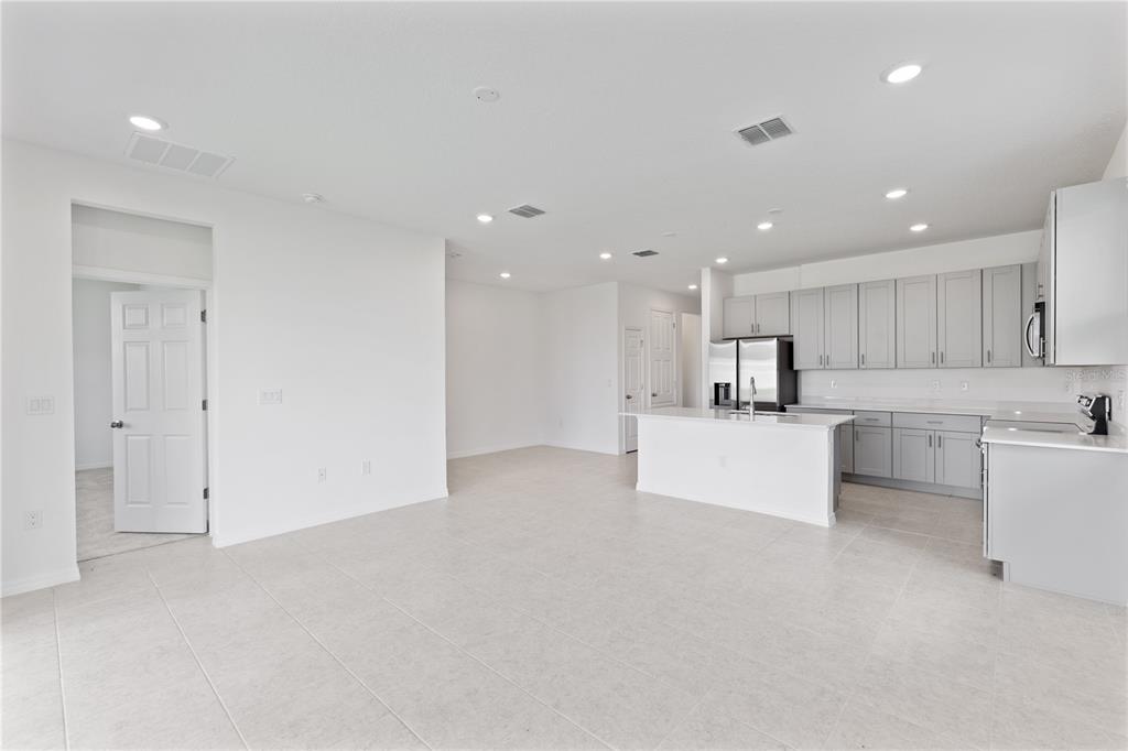 A bright, open-concept kitchen and living area featuring light gray cabinets and tile flooring — 491 SILVER PALM DRIVE, HAINES CITY, FL