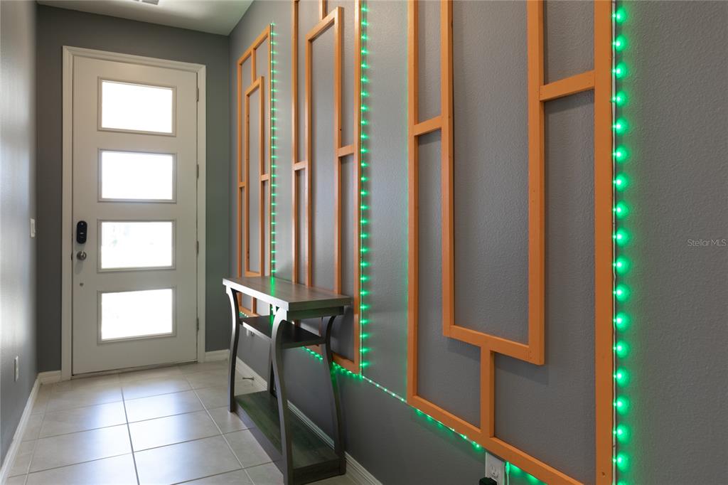 An entryway features a gray wall with orange geometric wood trim and green LED lighting — 2016 FLEMING MIST PLACE, KISSIMMEE, FL