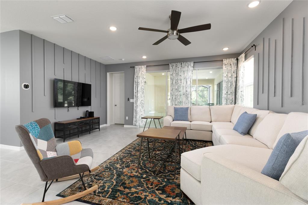 A living room features a sectional sofa, a rocking chair, and gray paneled walls — 2016 FLEMING MIST PLACE, KISSIMMEE, FL