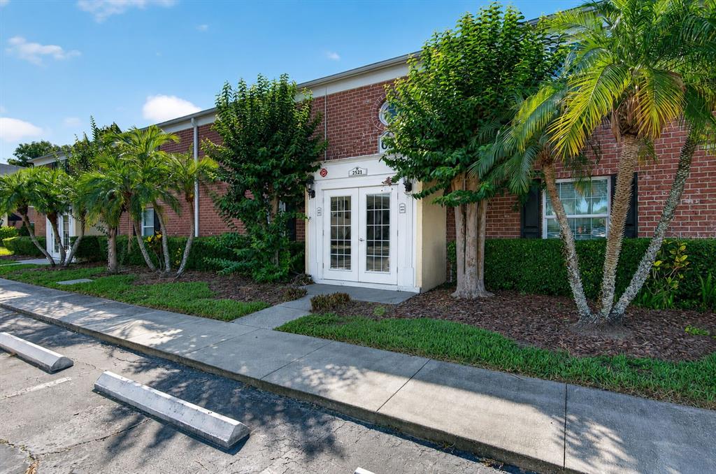 A brick building exterior features a white double-door entrance, palm trees, and a concrete sidewalk — 2521 CEDAR CYPRESS COURT UNIT 101, TAMPA, FL