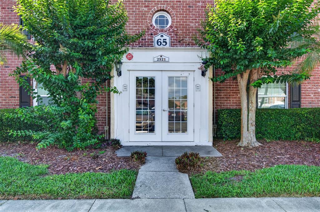 A brick building exterior features a white double-door entrance with a number 65 sign above — 2521 CEDAR CYPRESS COURT UNIT 101, TAMPA, FL
