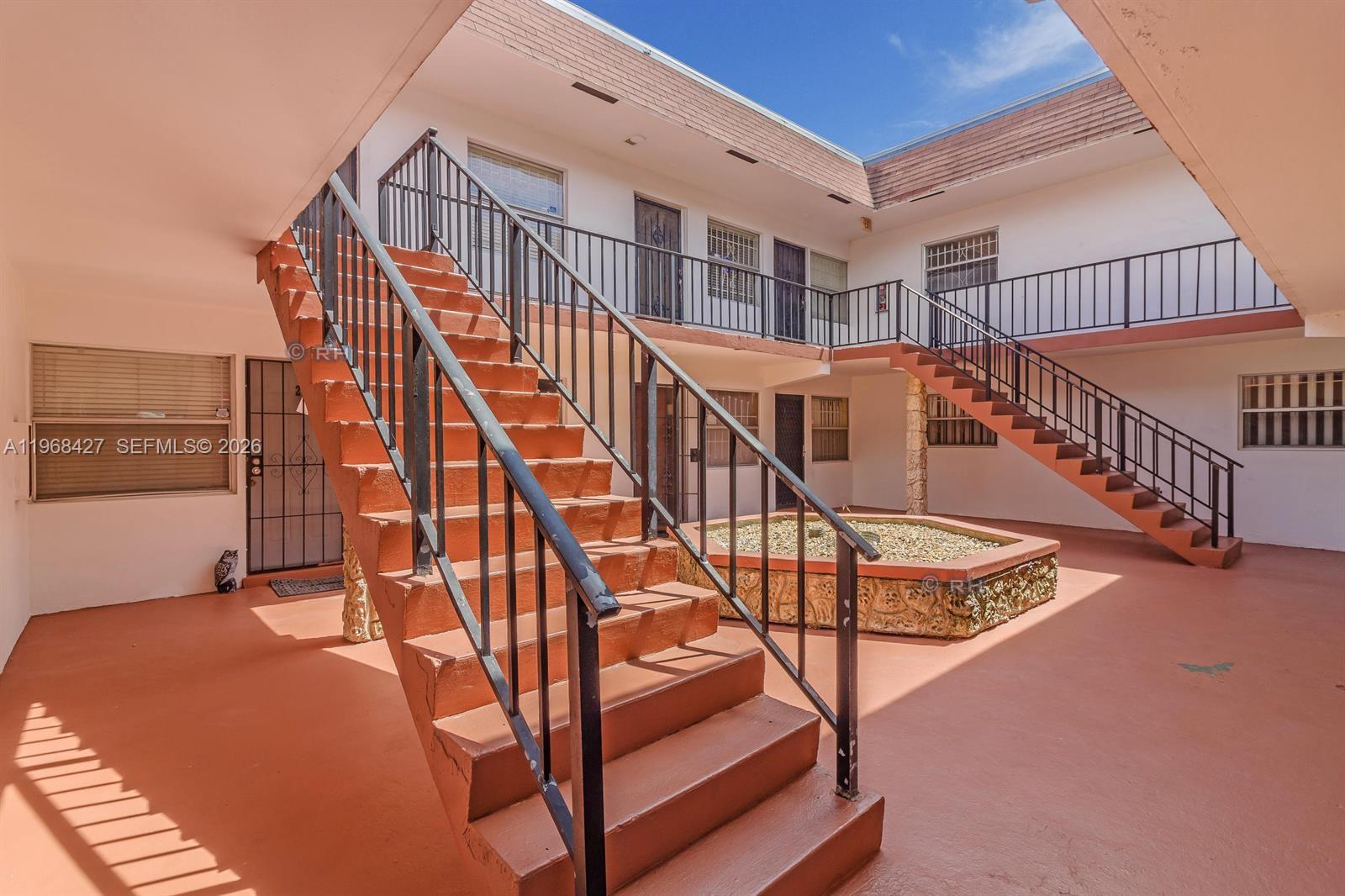 An outdoor courtyard features a central stone planter and two staircases leading to upper walkways — 344 SW 1st St # 6, Pompano Beach FL 33060, POMPANO BEACH, FL