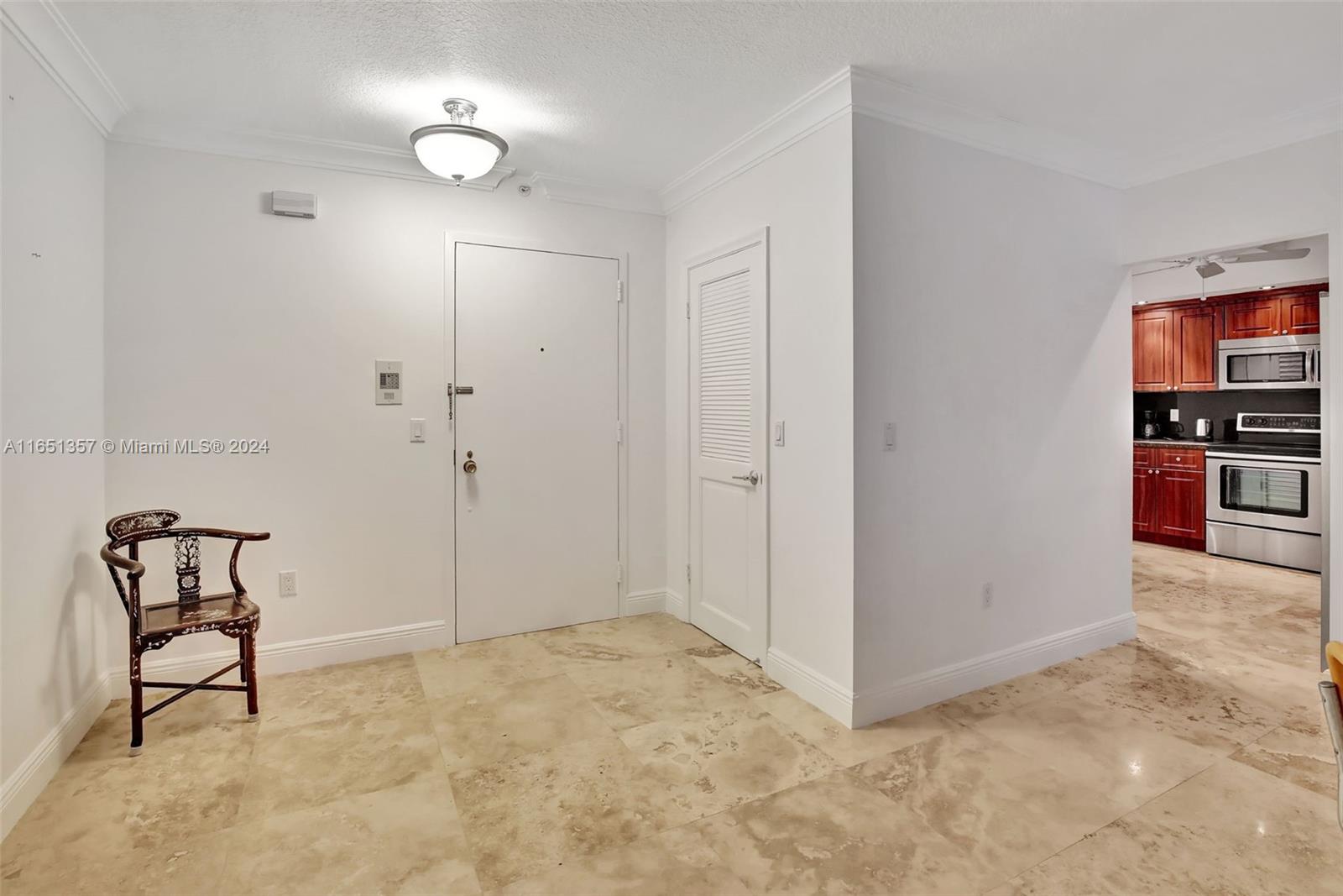 An entryway with a wooden chair, tiled floors, and a view into a kitchen — 9801 Collins Ave # 3T, Bal Harbour FL 33154, BAL HARBOUR, FL