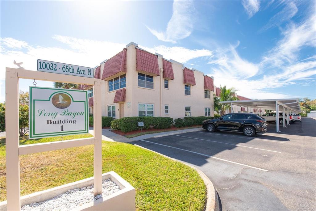 A multi-story apartment building with red awnings stands behind a sign in a parking lot — 10032 65TH AVENUE N UNIT 24, ST PETERSBURG, FL