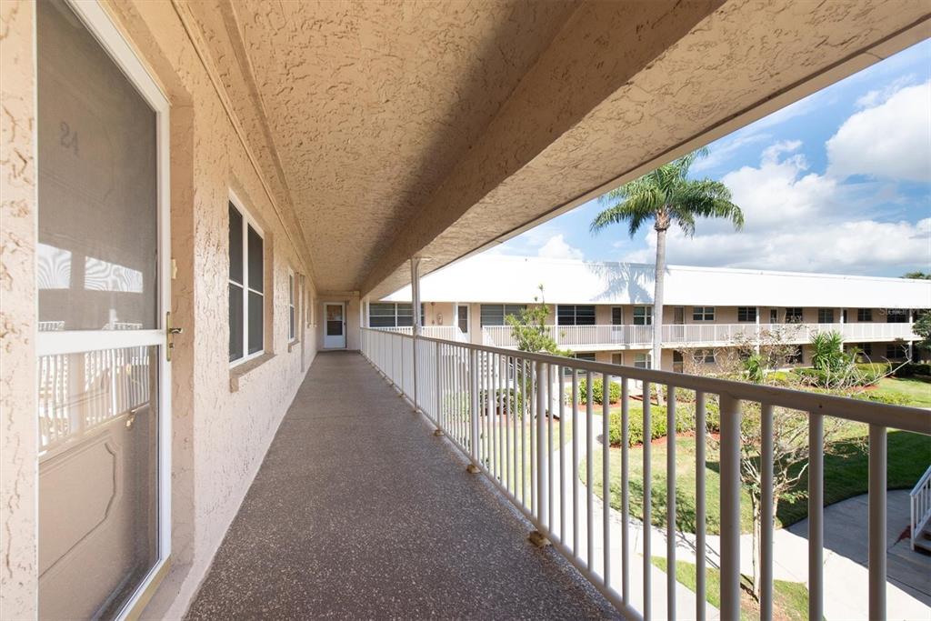 An outdoor covered walkway with a white metal railing overlooks a courtyard with palm trees — 10032 65TH AVENUE N UNIT 24, ST PETERSBURG, FL
