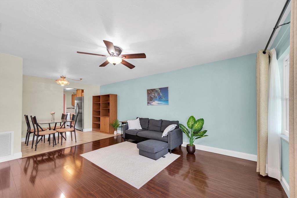 A living room with dark wood floors, a gray sofa, and an adjacent dining area — 10032 65TH AVENUE N UNIT 24, ST PETERSBURG, FL