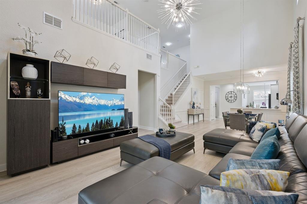 A spacious living room features a large television, gray sectional sofa, and a staircase — 6349 MIRAMONTE DRIVE UNIT 101, ORLANDO, FL