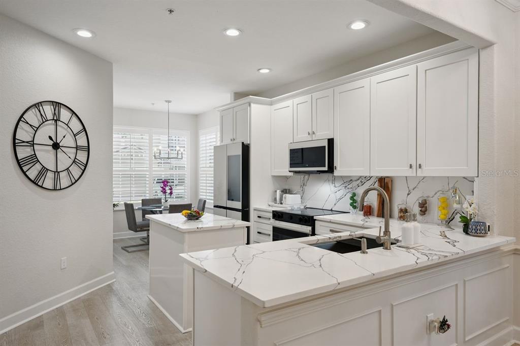 A modern kitchen features white cabinets, marble-look countertops, a center island, and an adjacent dining area — 6349 MIRAMONTE DRIVE UNIT 101, ORLANDO, FL