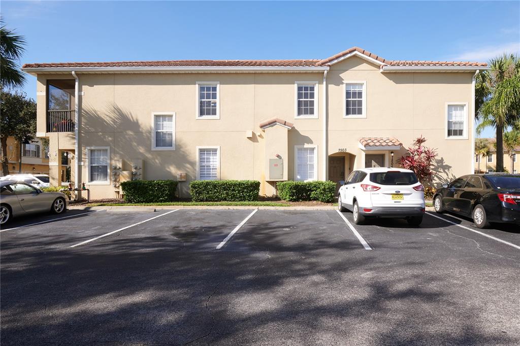 A two-story tan stucco apartment building with a tile roof and a parking lot — 7505 PELLHAM WAY, KISSIMMEE, FL
