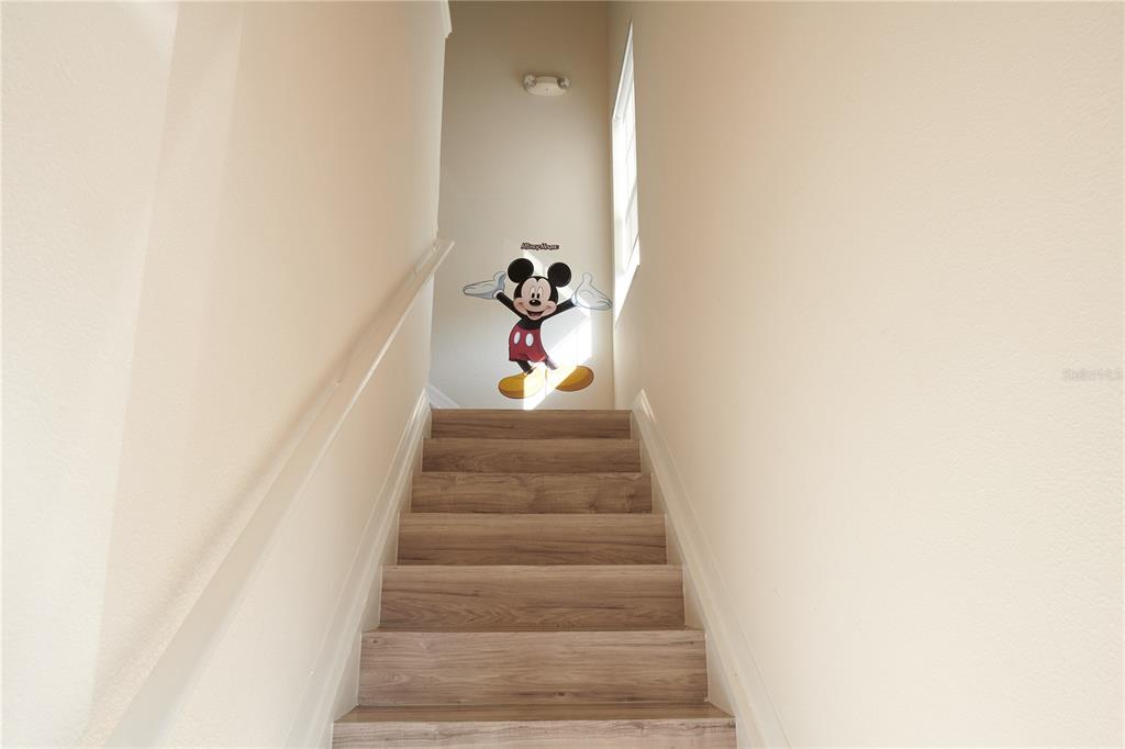 A staircase with wood-look steps leads to a landing featuring a Mickey Mouse wall decal — 7505 PELLHAM WAY, KISSIMMEE, FL