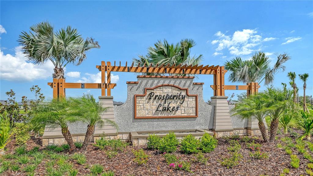 A stone monument sign for Prosperity Lakes stands in a landscaped area with palm trees — 11829 LILAC PEARL LANE, PARRISH, FL