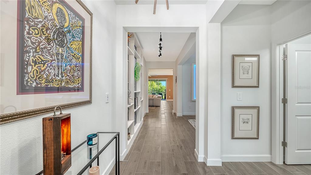 A hallway with wood-look tile flooring leads to an open living area with sliding doors — 11829 LILAC PEARL LANE, PARRISH, FL