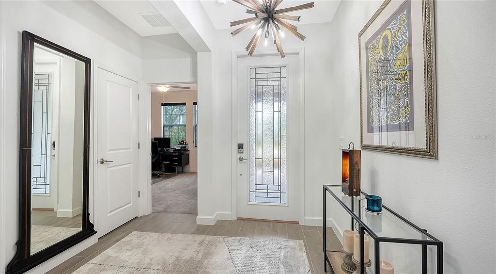 A bright entryway features a glass-paneled front door, a large floor mirror, and modern lighting — 11829 LILAC PEARL LANE, PARRISH, FL