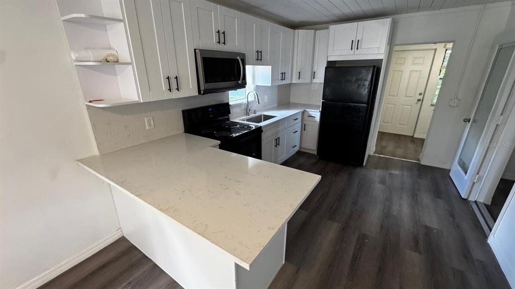 A kitchen features white cabinets, quartz countertops, a black refrigerator, and dark wood-look flooring — 345 AVENUE P NE, WINTER HAVEN, FL