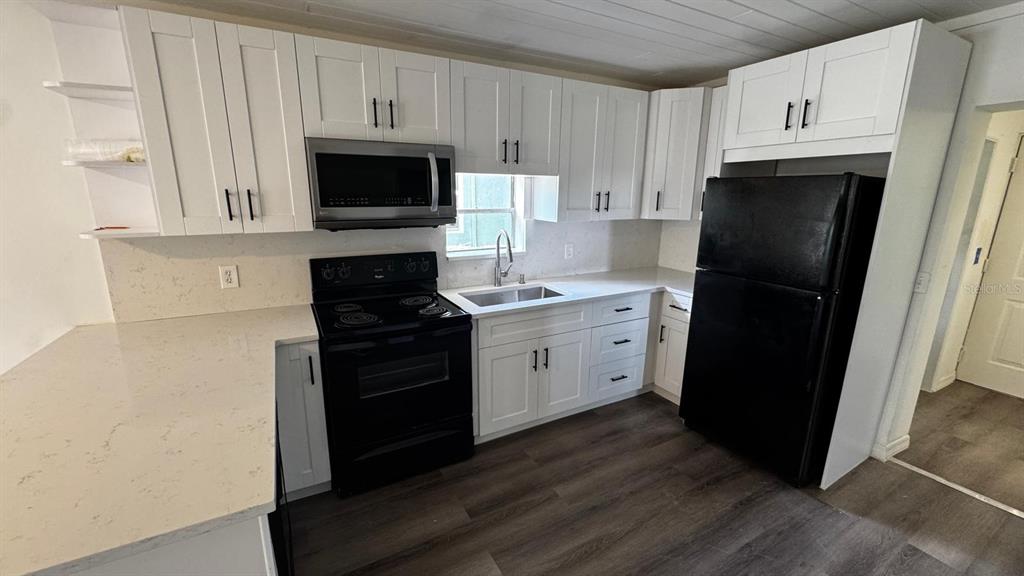 A kitchen features white cabinets, black appliances, quartz countertops, and wood-look flooring — 345 AVENUE P NE, WINTER HAVEN, FL