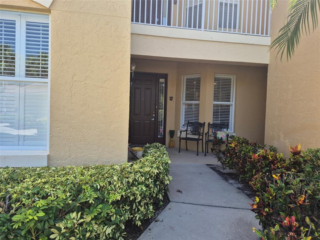 A walkway leads to the dark front door of a tan stucco building with landscaping — 7179 BOCA GROVE PLACE UNIT 101, BRADENTON, FL