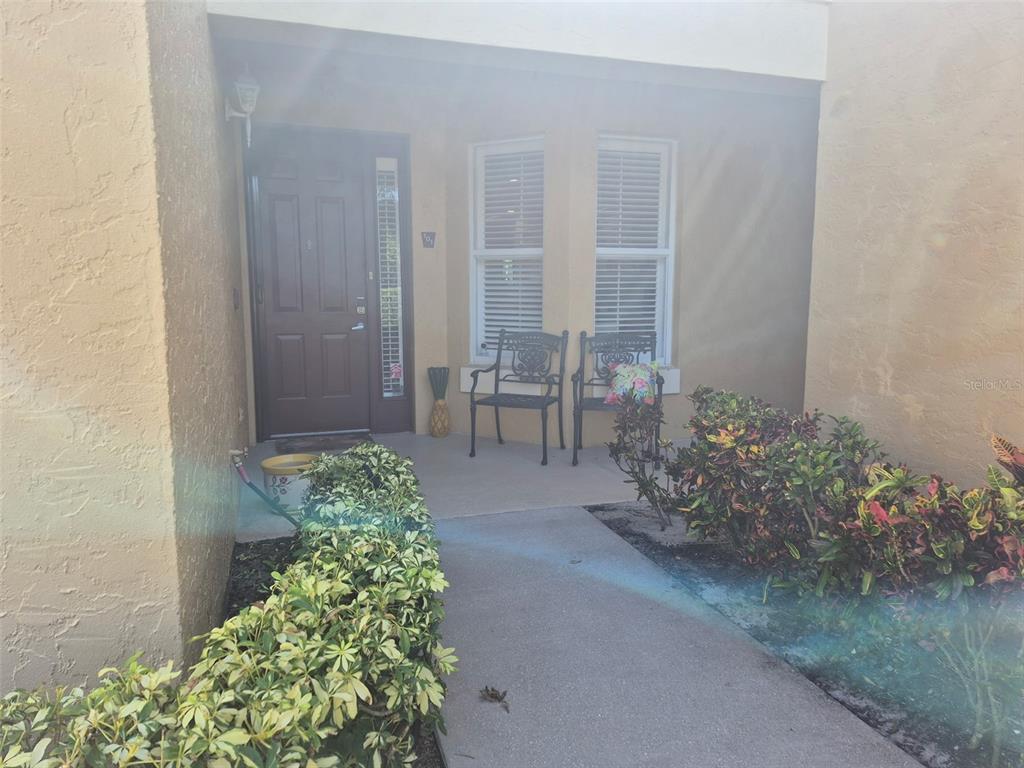 A concrete walkway leads to a covered entryway with a front door and two chairs — 7179 BOCA GROVE PLACE UNIT 101, BRADENTON, FL