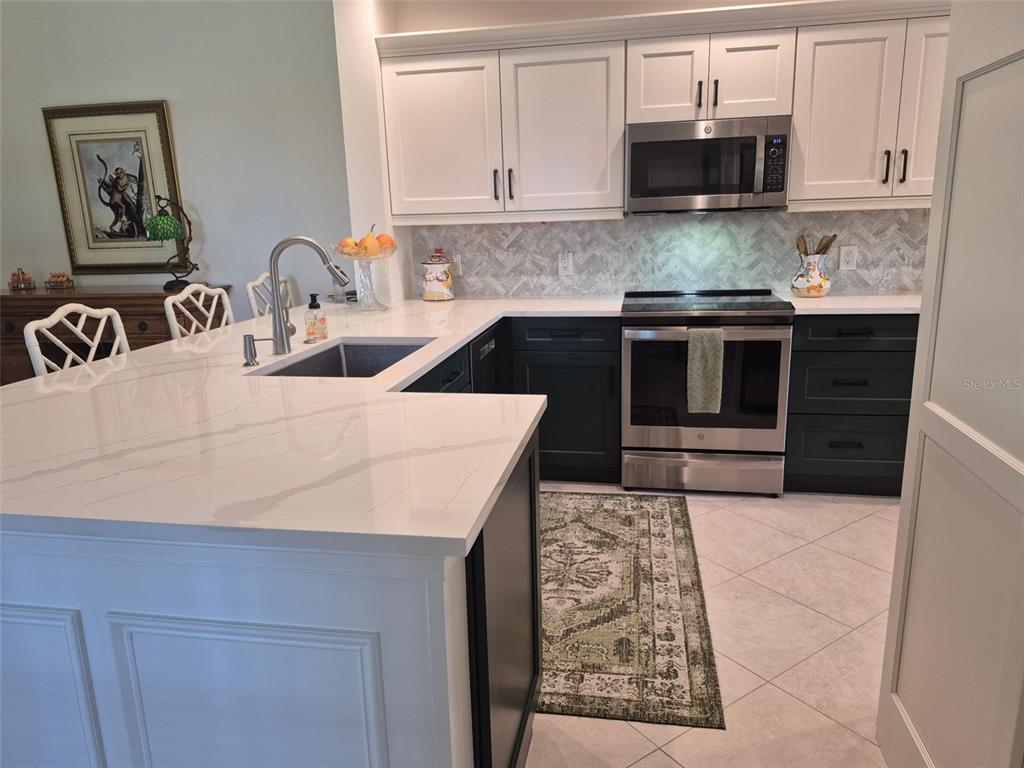 A kitchen features white upper cabinets, dark lower cabinets, a white island, and stainless appliances — 7179 BOCA GROVE PLACE UNIT 101, BRADENTON, FL
