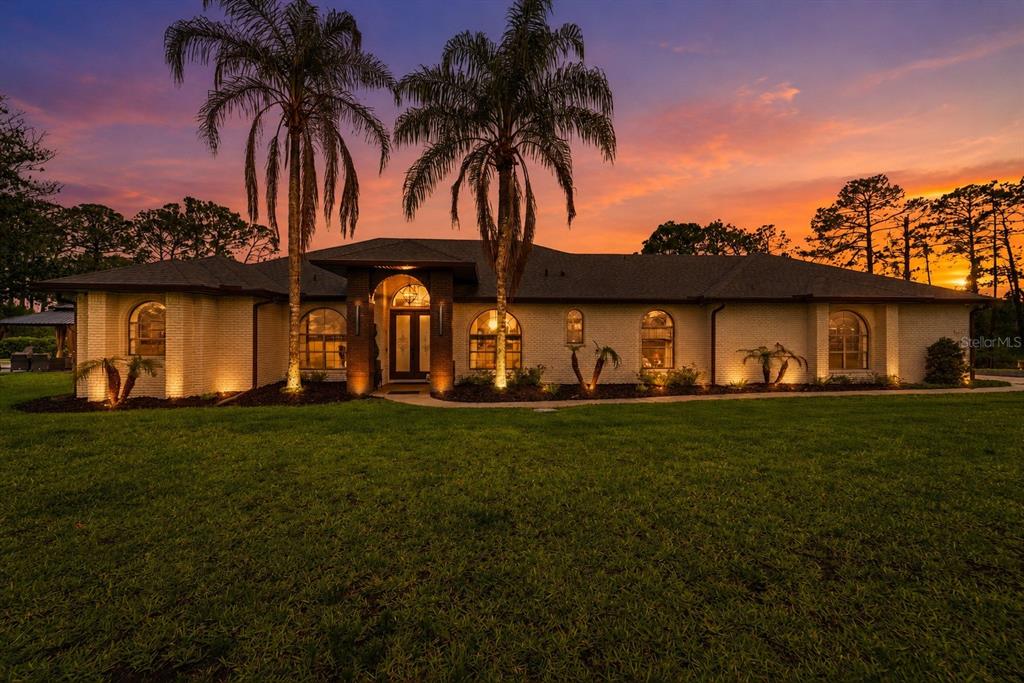 A single-story brick house with arched windows and two palm trees at sunset — 7025 S SYLVAN LAKE DRIVE, SANFORD, FL