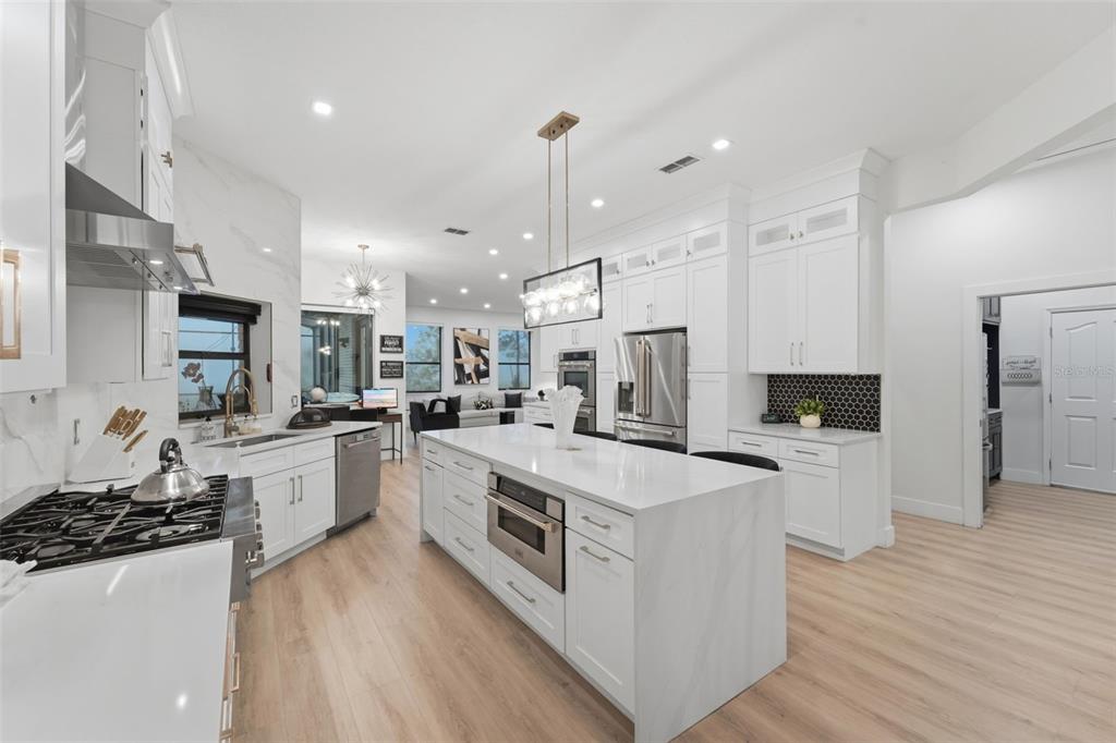 A modern white kitchen features a large waterfall island, stainless steel appliances, and light flooring — 7025 S SYLVAN LAKE DRIVE, SANFORD, FL