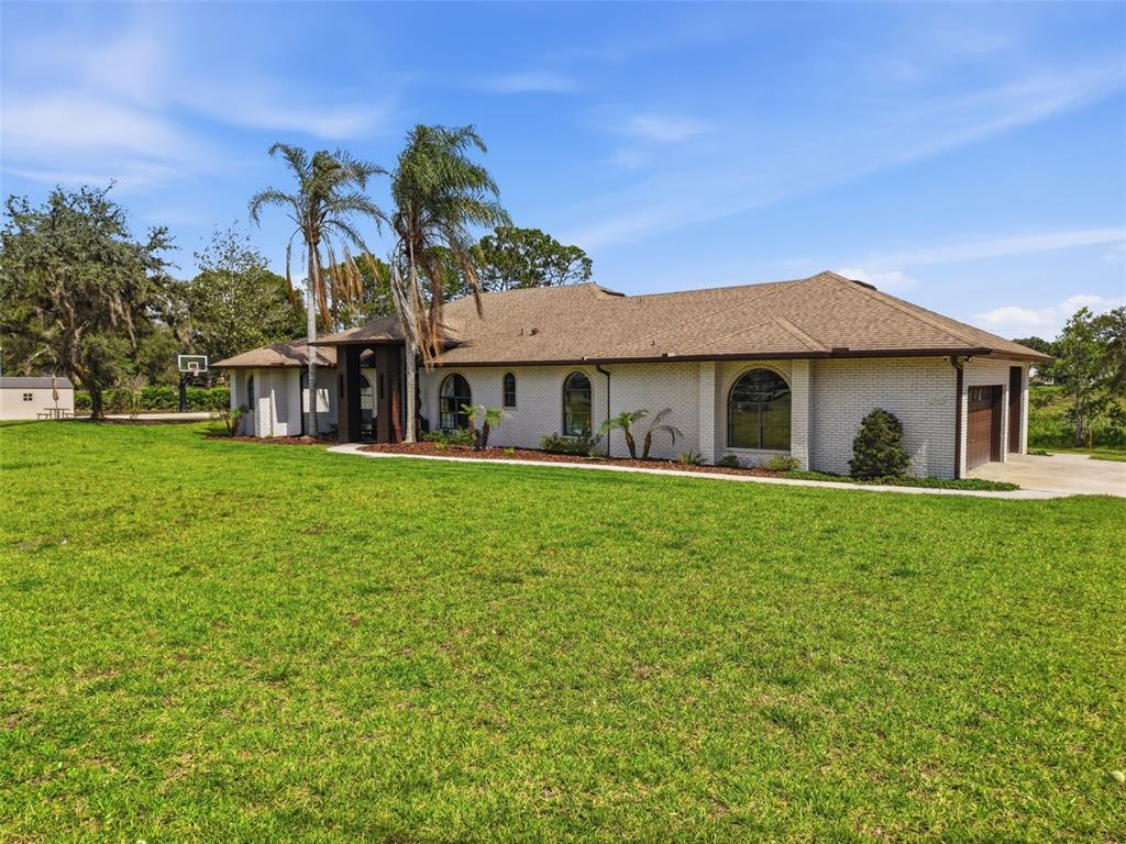 A single-story white brick house with a brown shingled roof sits on a grassy lawn — 7025 S SYLVAN LAKE DRIVE, SANFORD, FL