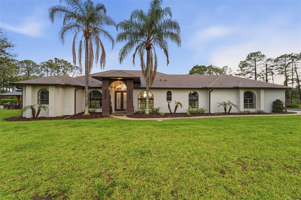 A single-story white brick house with arched windows and two palm trees in the front yard — 7025 S SYLVAN LAKE DRIVE, SANFORD, FL