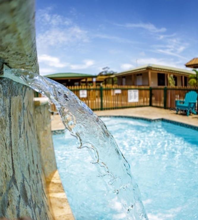 A stone water feature pours into a swimming pool with a wooden fence and building behind — B-13 CARR 3301 KM HM 1.9 INT STREET UNIT B-13, CABO ROJO, PR